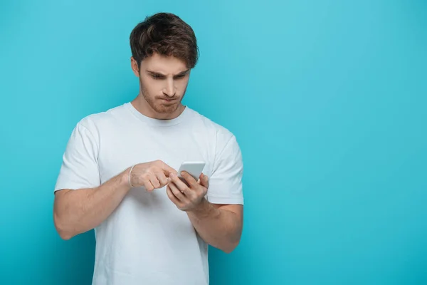 Konzentrierter junger Mann mit Smartphone auf blauem Hintergrund — Stockfoto