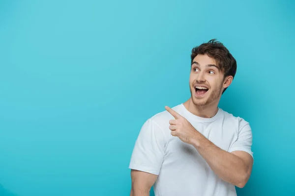 Sorprendido chico mirando hacia otro lado y señalando con el dedo sobre fondo azul - foto de stock