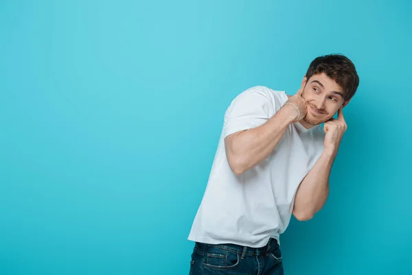 Displeased young man plugging ears with fingers while looking away on blue background — Stock Photo