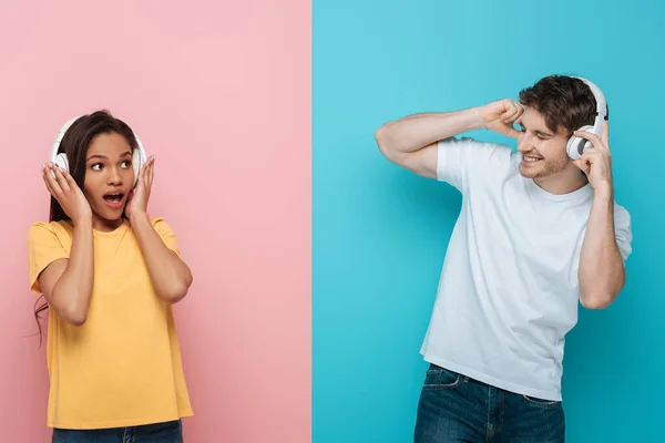 Collage aus schockiertem afrikanisch-amerikanischem Mädchen und aufgeregtem jungen Mann, der Musik in drahtlosen Kopfhörern auf blauem und rosa Hintergrund hört — Stock Photo