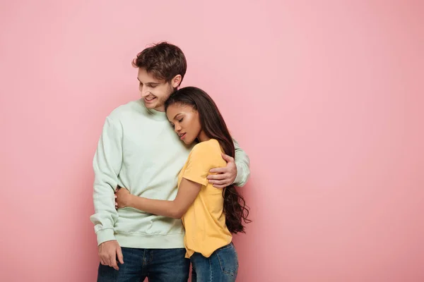 Attractive african american girl with closed eyes and happy guy embracing on pink background — Stock Photo