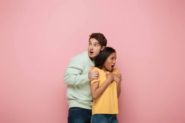 Scared man touching shoulders of frightened african american girlfriend on pink background — Stock Photo