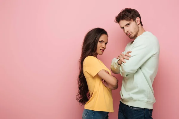 Offended interracial couple standing with crossed arms while looking at camera on pink background — Stock Photo