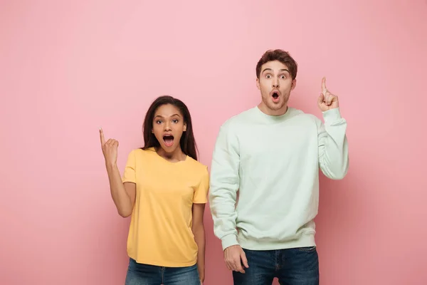 Excited interracial couple showing idea signs while looking at camera on pink background — Stock Photo