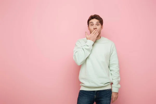 Schockierter Mann, der Mund mit der Hand bedeckt, während er in die Kamera auf rosa Hintergrund schaut — Stockfoto