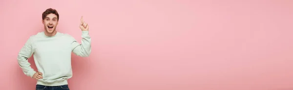 Panoramische Ernte des aufgeregten Kerls, der Ideenschild zeigt, während er mit der Hand auf der Hüfte steht und in die Kamera auf rosa Hintergrund schaut — Stockfoto