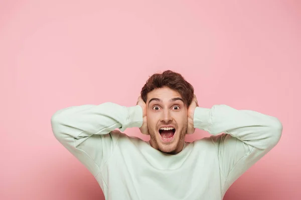 Hombre asustado gritando mientras cubre las orejas con las manos sobre fondo rosa - foto de stock