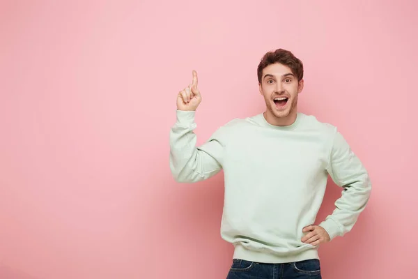 Gars excité montrant signe idée tout en se tenant avec la main sur la hanche et en regardant la caméra sur fond rose — Photo de stock