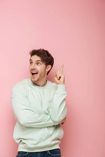 Eccitato giovane in piedi con la bocca aperta e mostrando idea gesto su sfondo rosa — Foto stock