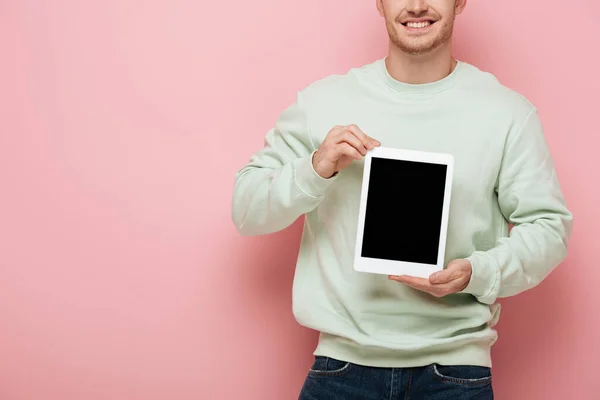 Vista parcial del hombre sonriente mostrando tableta digital con pantalla en blanco sobre fondo rosa - foto de stock