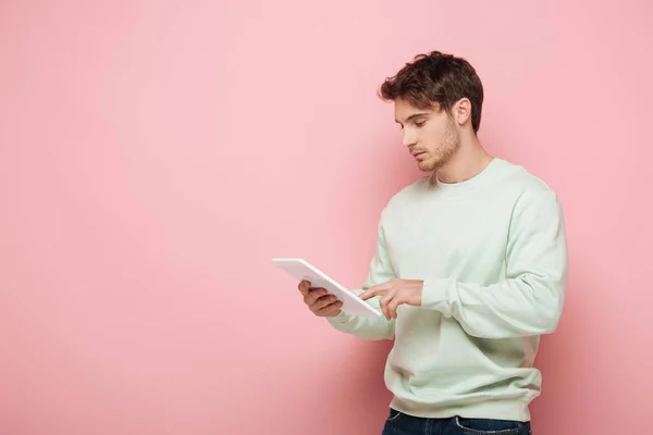 Concentrated young man using digital tablet on pink background — Stock Photo