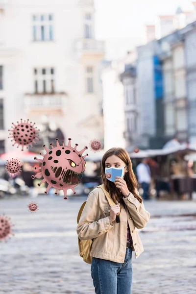 Belle femme en masque médical regardant l'illustration de bactéries en colère dans la rue — Photo de stock