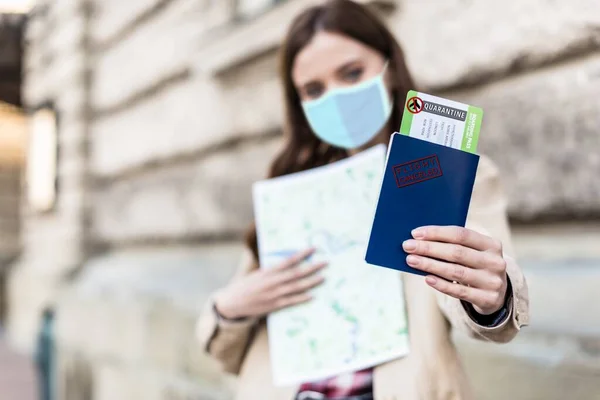 Selective focus of woman in medical mask holding map and showing passport and air ticket with quarantine illustration — Stock Photo