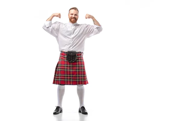 Smiling Scottish redhead man in red kilt showing muscles on white background — Stock Photo