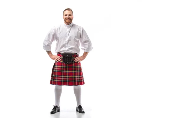 Sorrindo escocês ruiva homem em kilt vermelho com as mãos em quadris no fundo branco — Fotografia de Stock