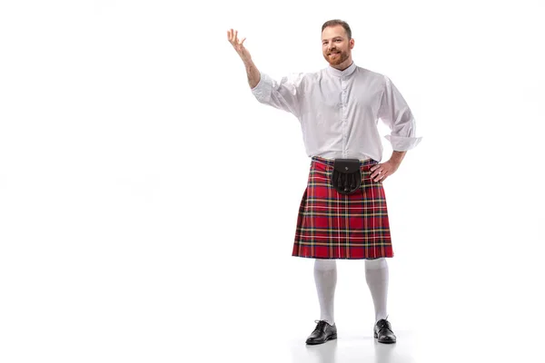 Lächelnder schottischer Rotschopf im roten Kilt, der mit der Hand auf weißem Hintergrund zeigt — Stockfoto