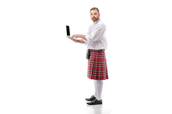 Scottish redhead man in red kilt holding laptop on white background — Stock Photo