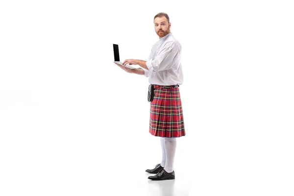 Scozzese rossa uomo in kilt rosso che tiene il computer portatile su sfondo bianco — Foto stock