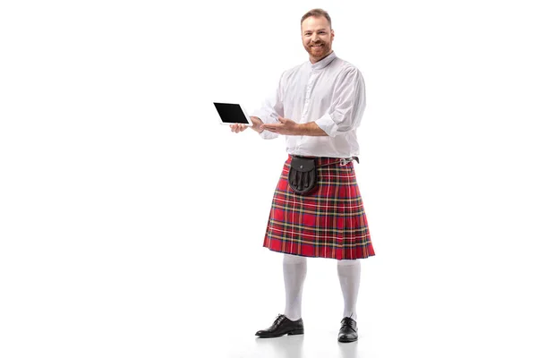 Homme rousse écossais souriant en kilt rouge avec tablette numérique sur fond blanc — Photo de stock