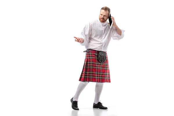 Displeased Scottish redhead man in red kilt talking on digital tablet on white background — Stock Photo