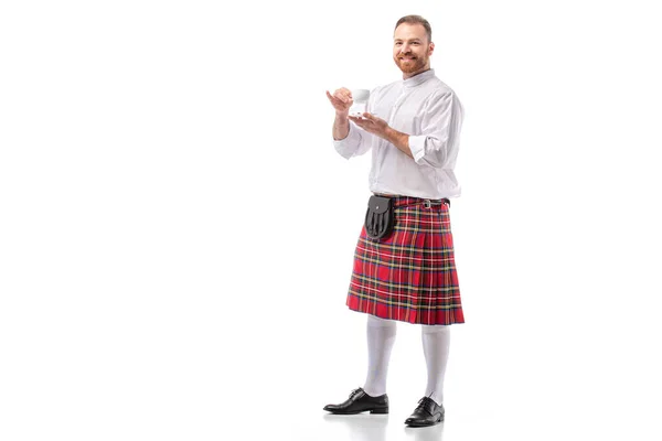 Lächelnder schottischer Rotschopf im roten Kilt, der Kaffee auf weißem Hintergrund trinkt — Stockfoto