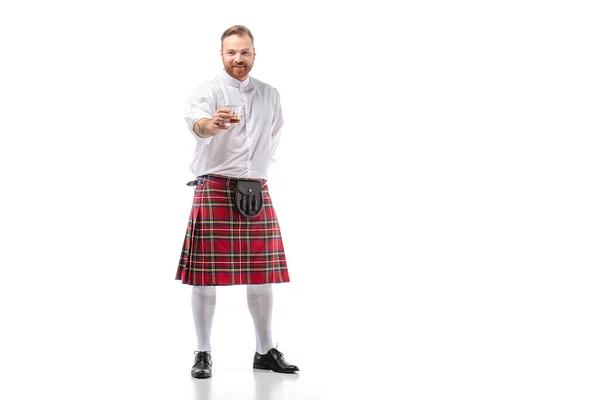 Sorridente escocês ruiva homem em kilt vermelho com uísque em vidro sobre fundo branco — Fotografia de Stock