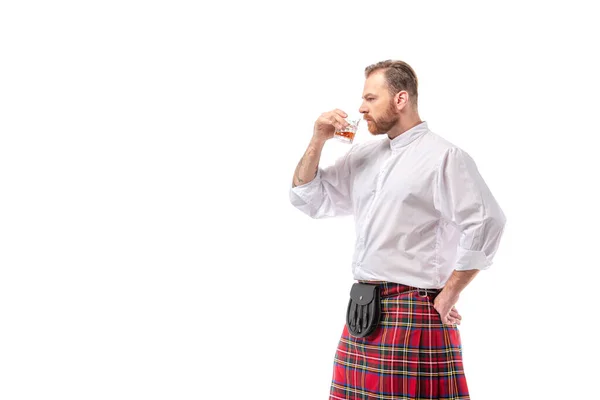 Шотландский рыжий человек в красном килте, нюхающий виски изолированный на белом — стоковое фото