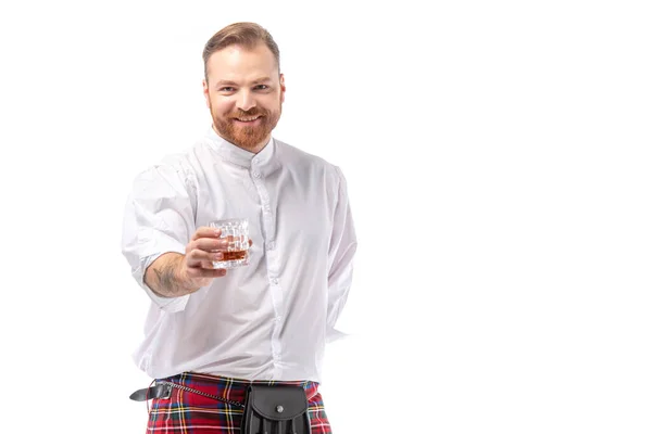 Sorridente escocês ruivo homem em kilt vermelho com uísque em vidro isolado em branco — Fotografia de Stock
