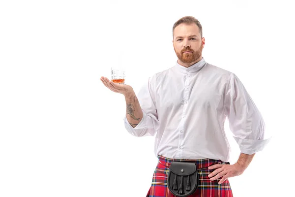 Scottish redhead man in red kilt with whiskey in glass on hand isolated on white — Stock Photo
