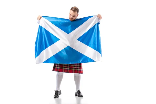 Scottish redhead man in red kilt looking at flag of Scotland on white background — Stock Photo