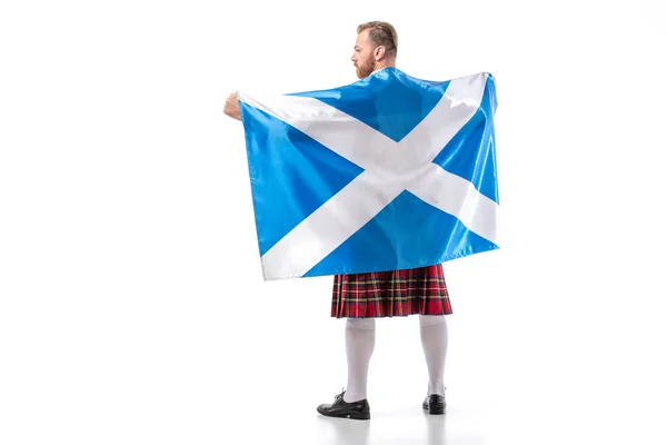 Visão traseira do homem ruivo escocês em kilt vermelho com bandeira da Escócia no fundo branco — Fotografia de Stock