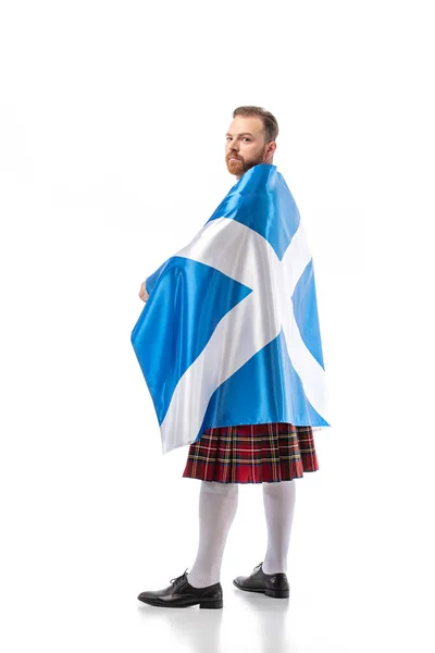 Visão traseira do homem ruivo escocês em kilt vermelho com bandeira da Escócia no fundo branco — Fotografia de Stock