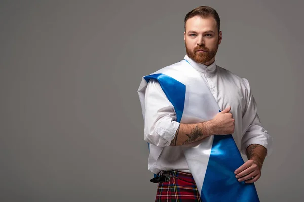 Grave escocês ruiva homem em kilt vermelho com bandeira da Escócia em fundo cinza — Fotografia de Stock