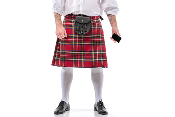 Vista recortada del hombre escocés en escocés rojo con bolsa de cinturón de cuero y teléfono inteligente sobre fondo blanco - foto de stock