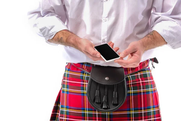 Vista cortada do escocês homem em kilt vermelho com bolsa de cinto de couro e smartphone isolado no branco — Fotografia de Stock