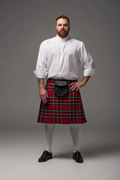 Écossais rousse homme en kilt rouge avec la main sur la hanche sur fond gris — Photo de stock