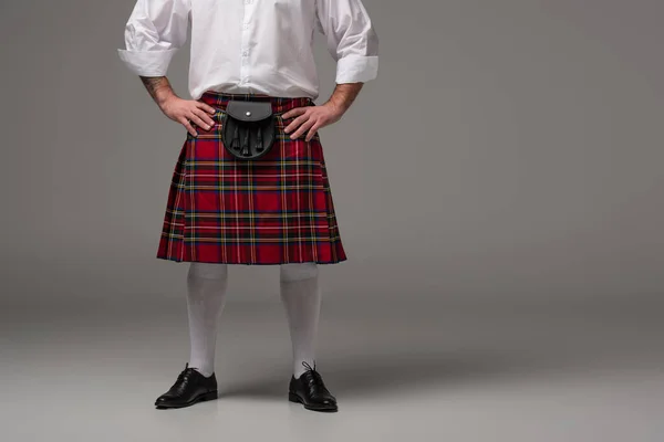 Cropped view of Scottish man in red kilt with hands on hips on grey background — Stock Photo