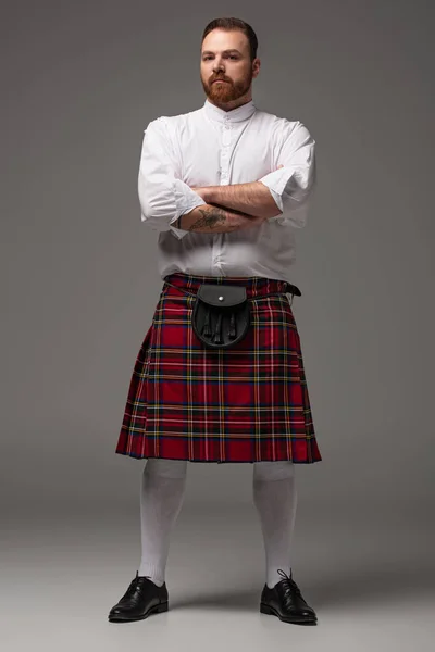 Escocês ruiva homem em kilt vermelho com braços cruzados no fundo cinza — Fotografia de Stock