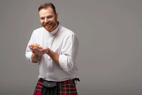 Happy Scottish redhead man in red kilt with gold coins on grey background — Stock Photo