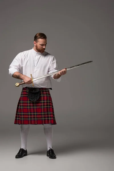 Schottischer Rotschopf im roten Kilt mit Schwert auf grauem Hintergrund — Stockfoto