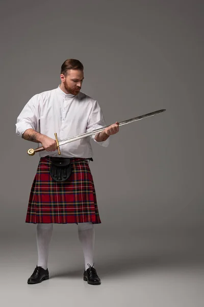 Escocês ruiva homem em kilt vermelho com espada no fundo cinza — Fotografia de Stock