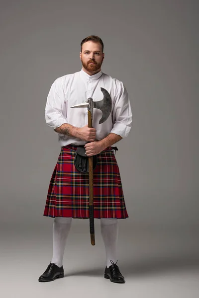 Scottish redhead man in red kilt with battle axe on grey background — Stock Photo