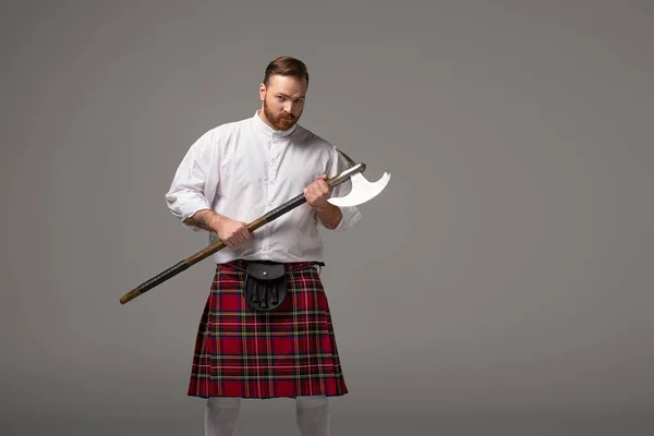 Ernster schottischer Rotschopf im roten Kilt mit Kampfbeil auf grauem Hintergrund — Stockfoto