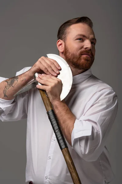 Scottish redhead man shaving beard with battle axe on grey background — Stock Photo