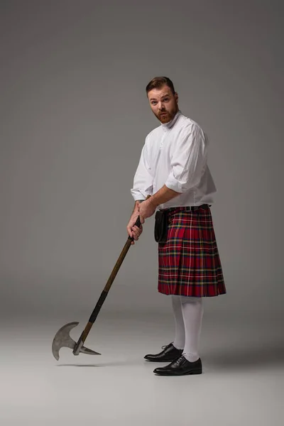 Escocês ruiva homem em kilt vermelho com machado de batalha no fundo cinza — Fotografia de Stock