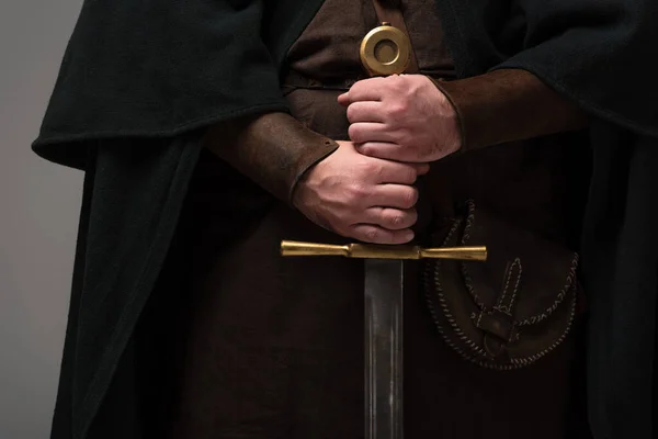 Cropped view of medieval Scottish knight with sword in hands on grey background — Stock Photo