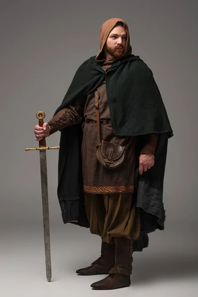 Mittelalterlicher schottischer Rotschopfritter im Mantel mit Schwert auf grauem Hintergrund — Stockfoto