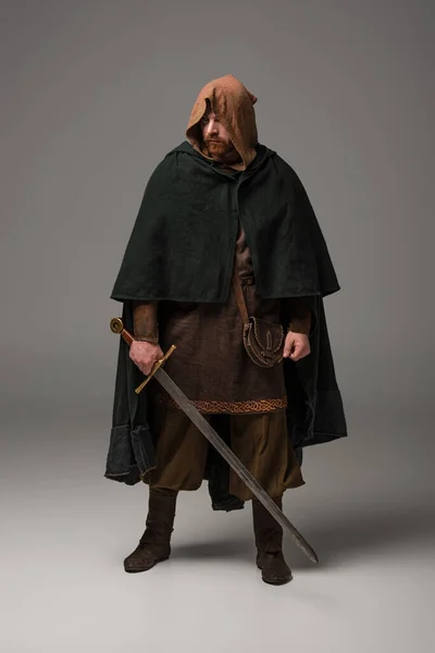 Medieval escocés pelirroja caballero en mantel con espada sobre fondo gris - foto de stock