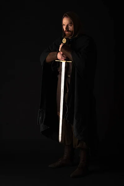 Medieval Scottish man in mantel with sword in dark isolated on black — Stock Photo