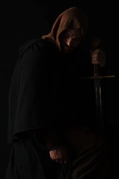 Середньовічний шотландський чоловік у мантелі з мечем у темряві ізольований на чорному — стокове фото